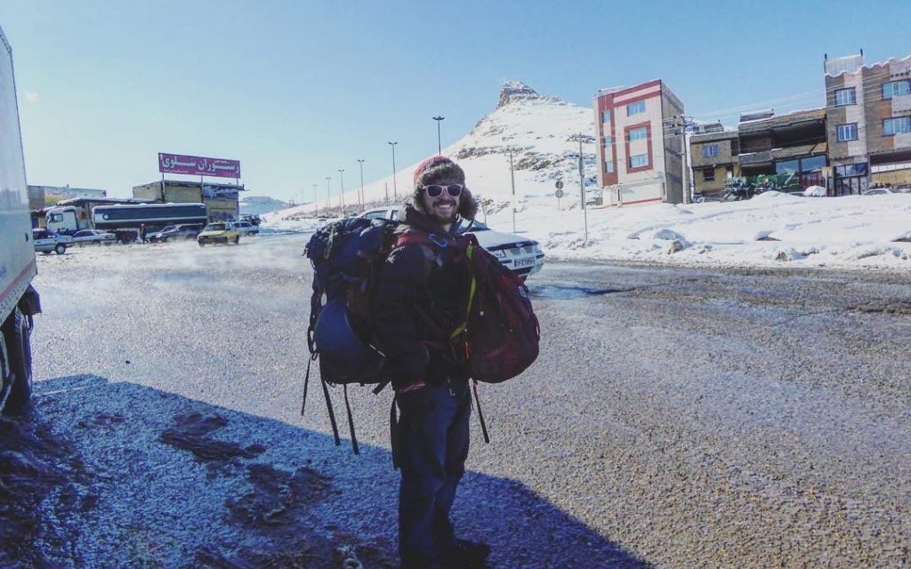 man with two backapacking backpacks getting ready to hitchhike in iran in winter while travelling overland