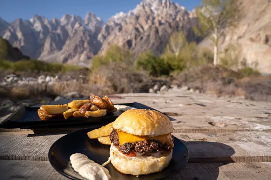A yak burger is sitting on a plate with mountains behind it in Pakistan