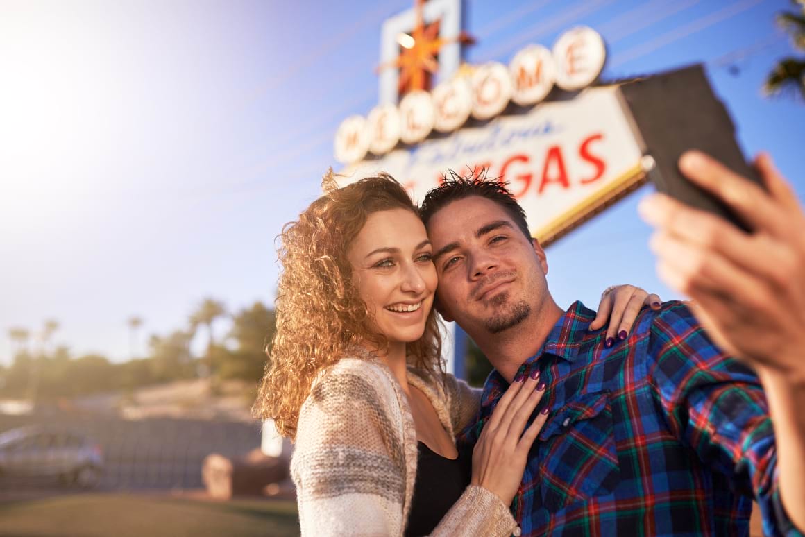 couple taking selfie by welcome to las vegas sign