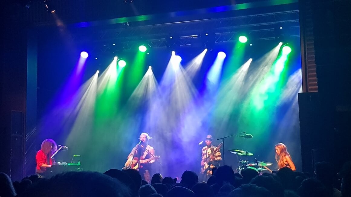 Music festival stage with green and white stage lights and four band members