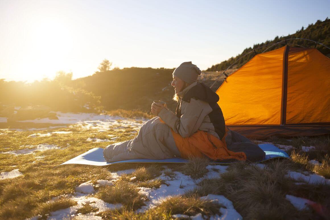 woman camping in sleeping bag with hot drink