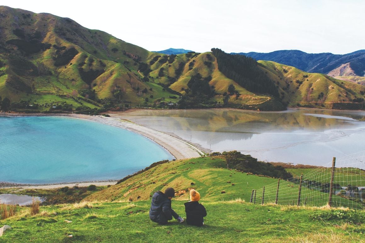 Kids sitting in an expansive valley in front of a panoramic vista of Cable Bay in Nelson, New Zealand.