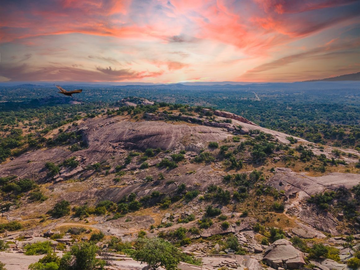 A pink granite dome with lush landscape in the background at Enchanted Rock State Natural Area, Fredericksburg