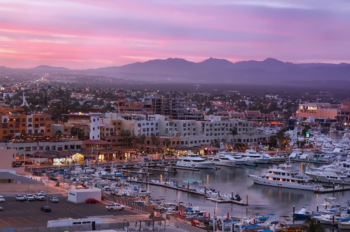 Los Cabos Marina's Harbor during sunset: yachts, cityscpae and mountains in the background  