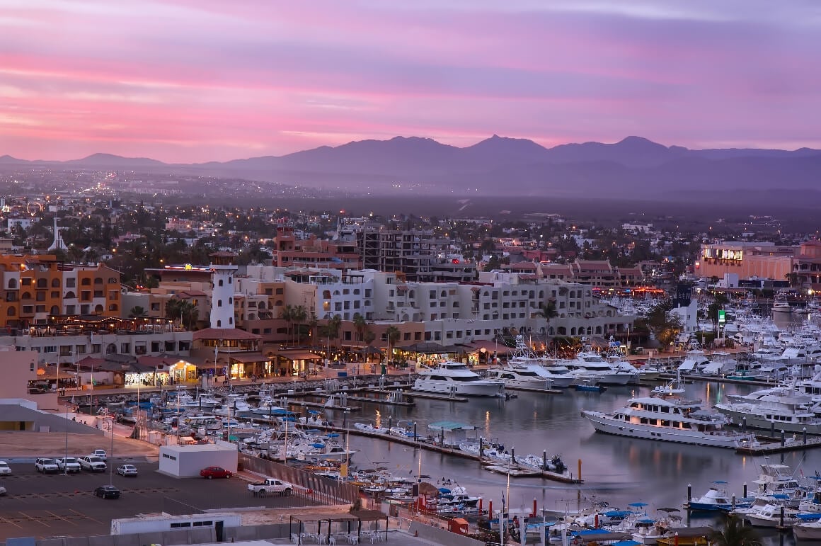 Los Cabos Marina's Harbor during sunset: yachts, cityscpae and mountains in the background
