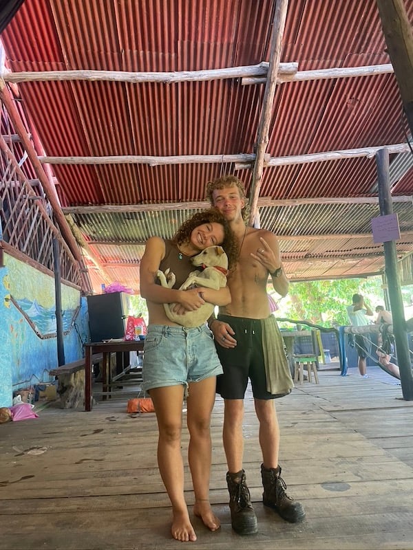 Two friends at a hostel holding a dog and smiling in the communal area