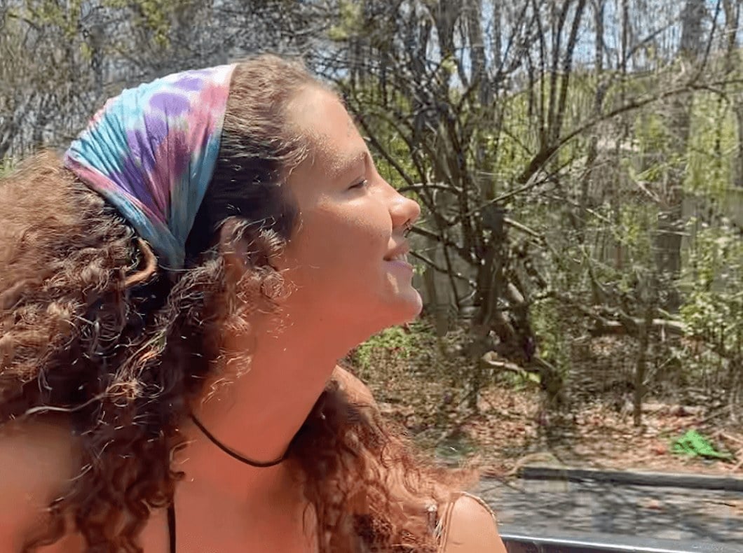 A side-profile photo of a girl with a scarf wrapped around her head, breathing in the beautiful views around her 