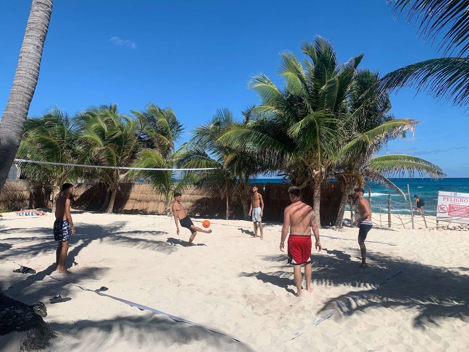 5 people playing football on the white sand. Palm tree and turquoise waters in the background. Isla Mujeres, Mexico. 