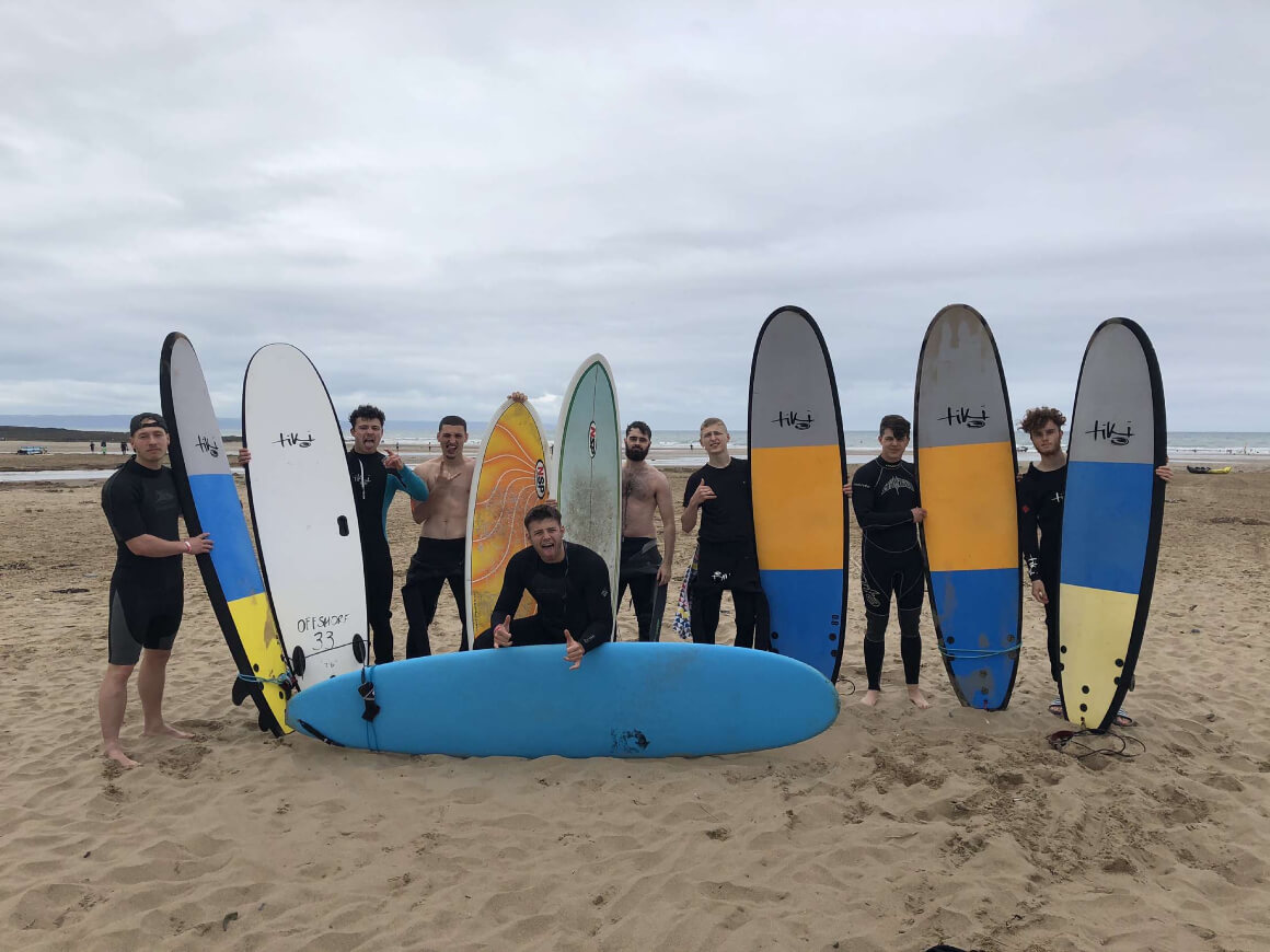 Group of people in wetsuits standing with surf boards on the beach