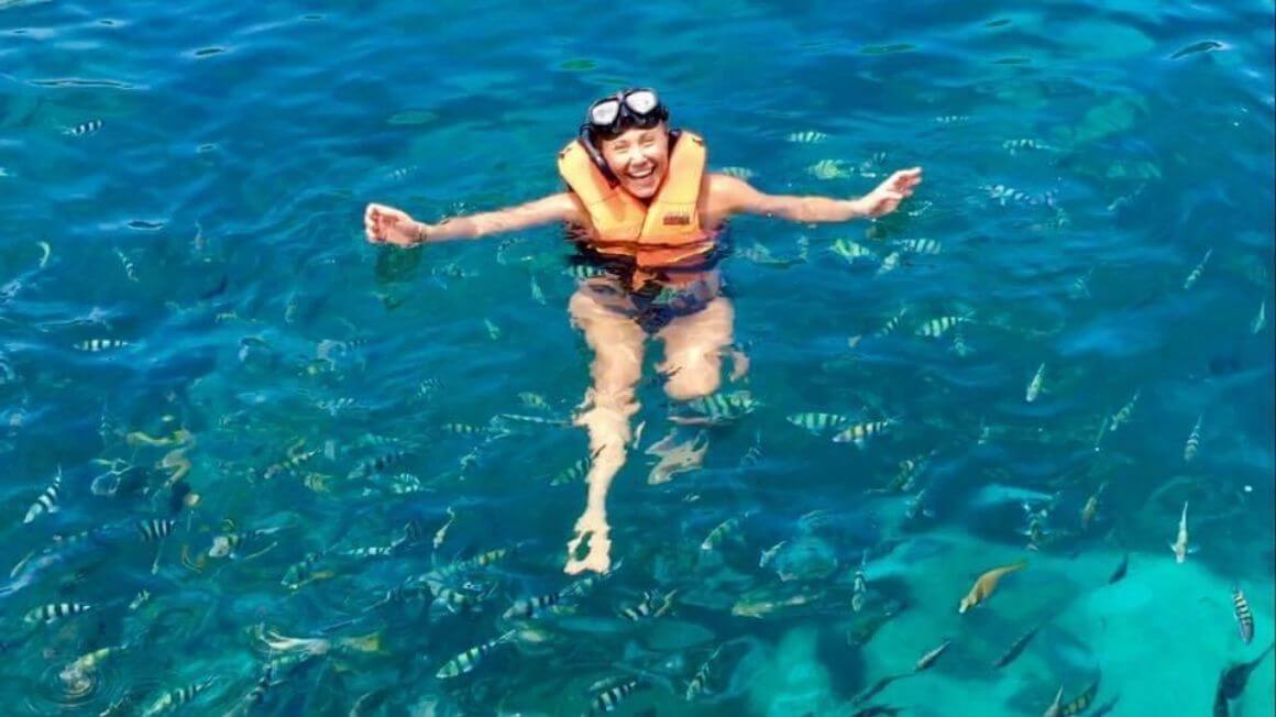 Girl snorkelling is beautiful blue water surrounded by stripey fish. 