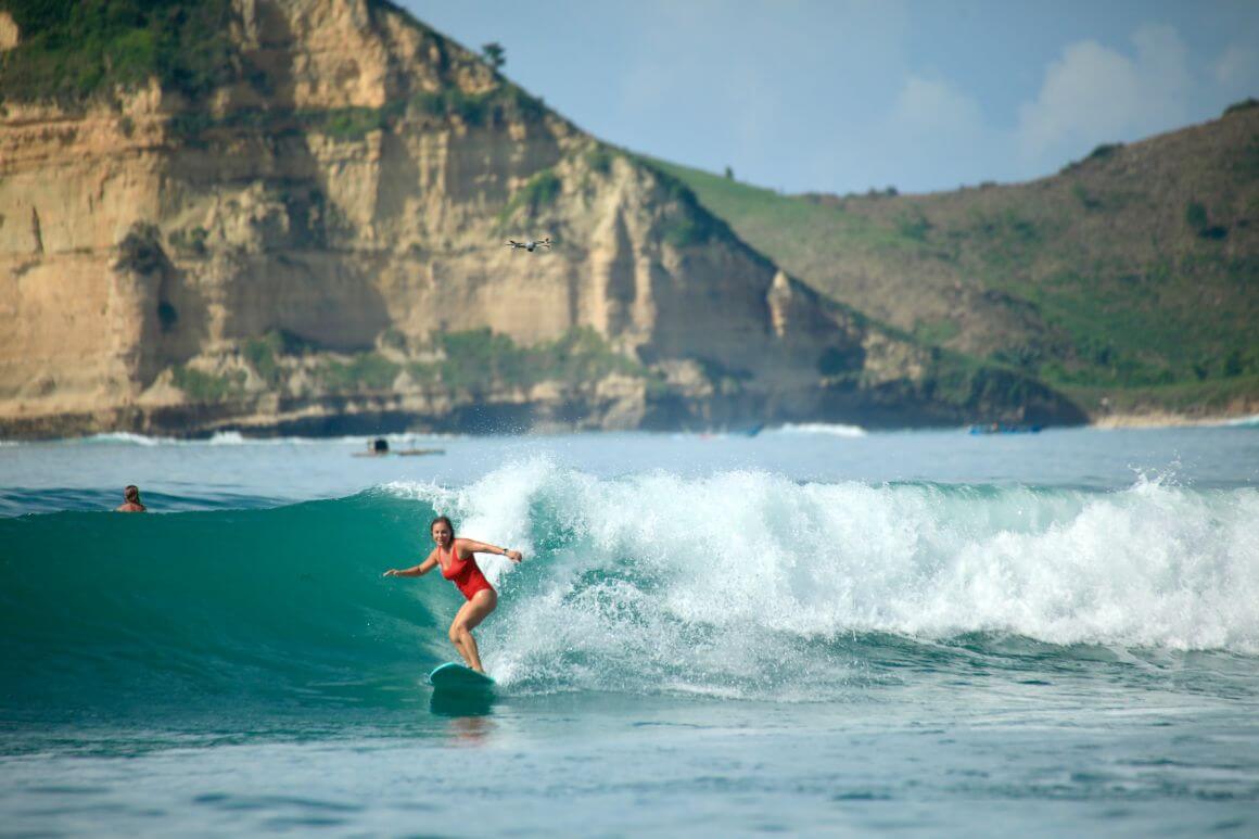 Women (Max) with a red bathing suite surfing a wave in Lombok with mountains in the background