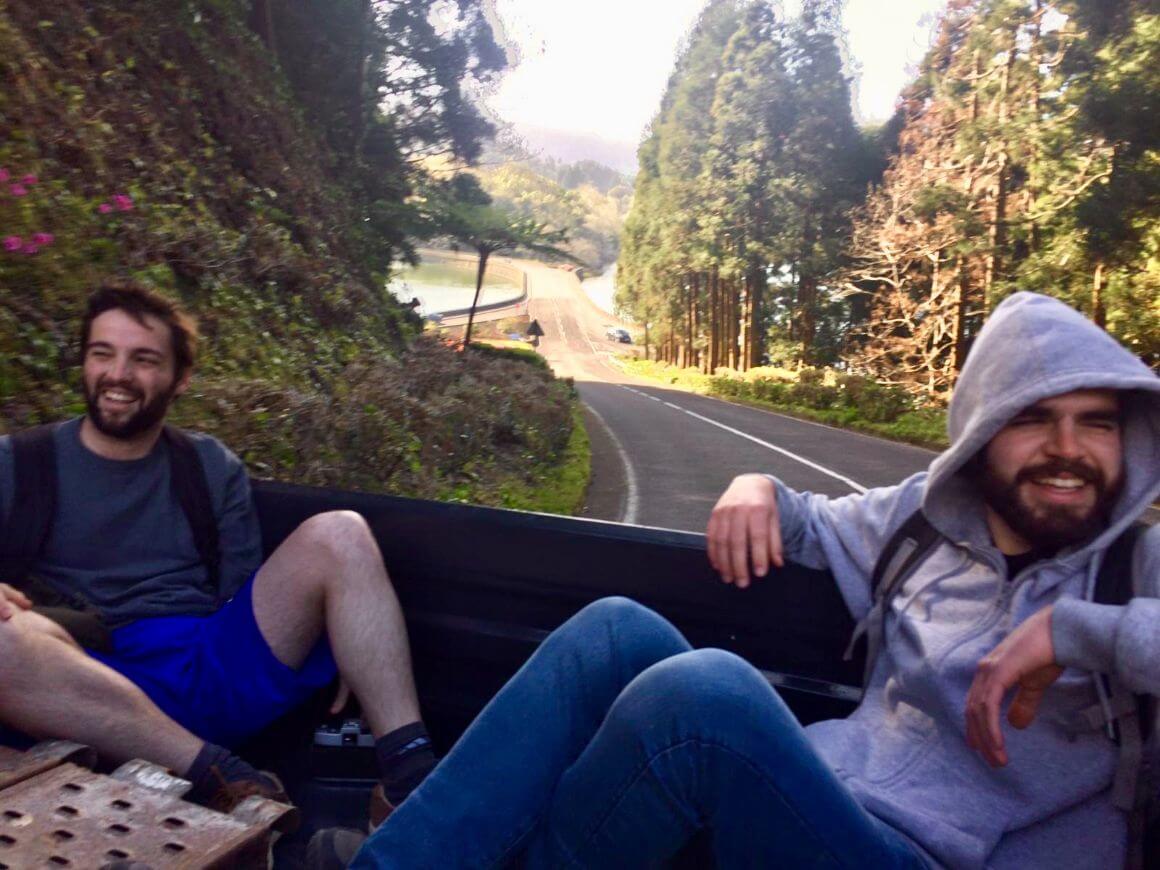 Two people smiling in the back of a pick up truck on the road