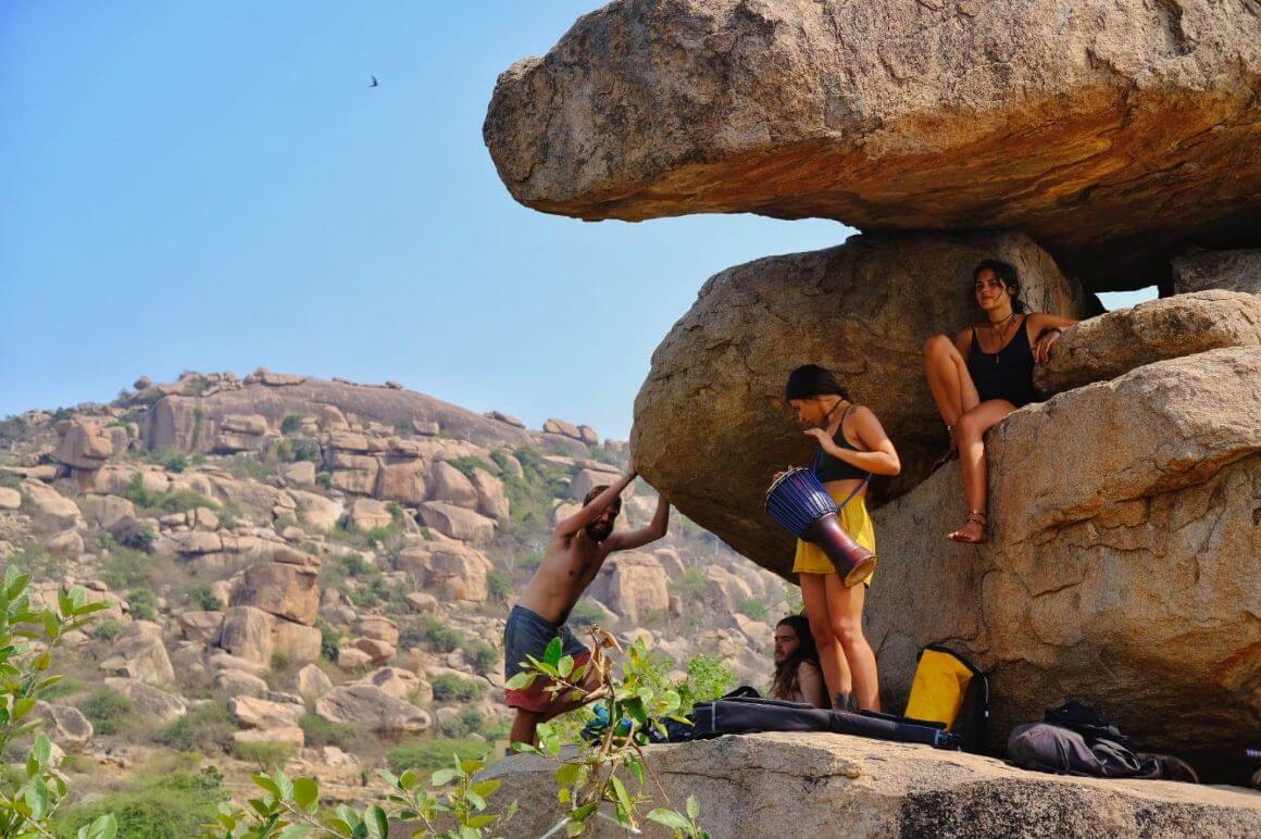 friends hang out playing music on the boulders in hampi, india