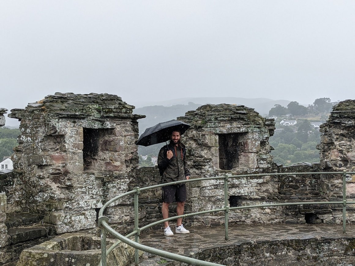 A person stood on ruins in the rain with an umbrella 