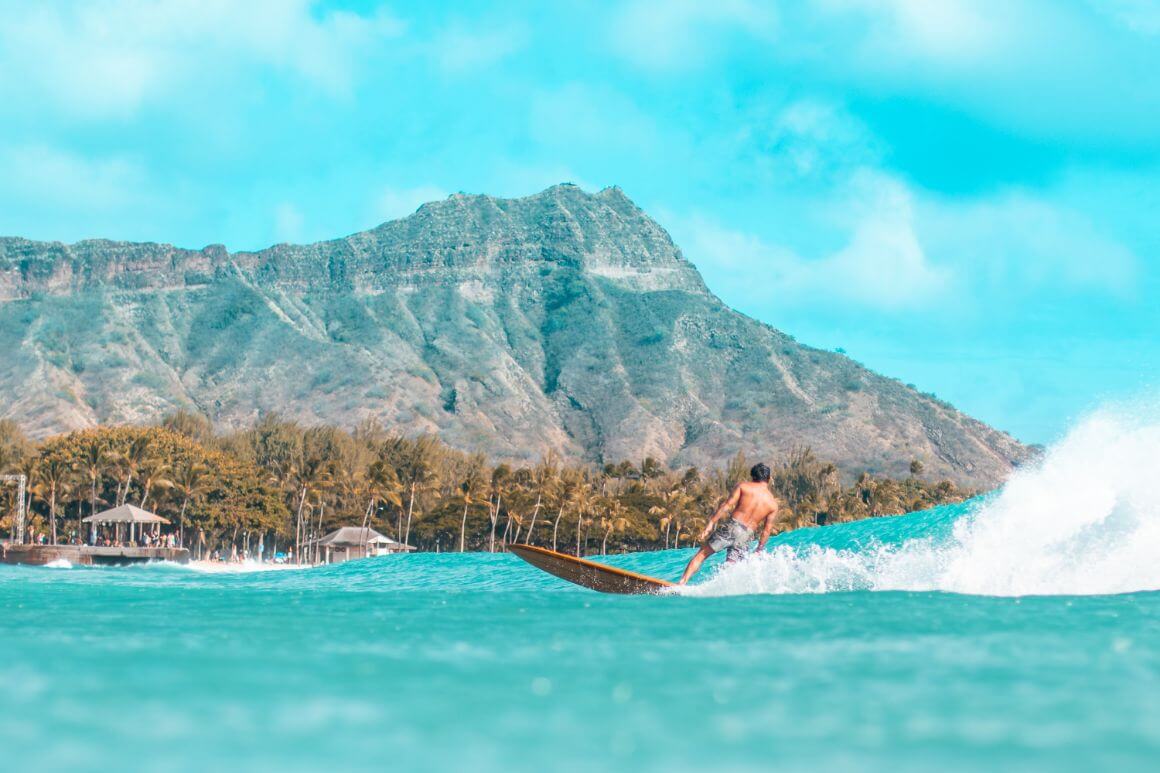 A man surfing in Oahu, Hawaii with views of lush forest and mountains.