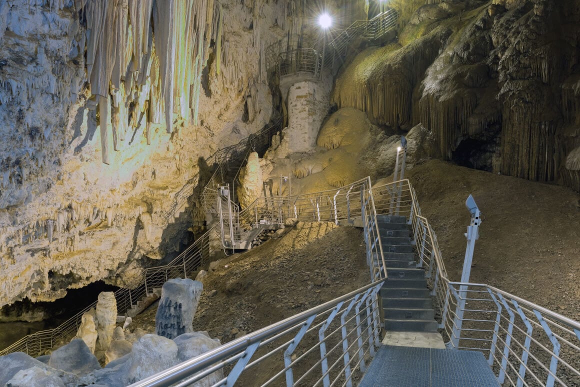 Staircase leading into a dark cave with geological formations in Antiparos