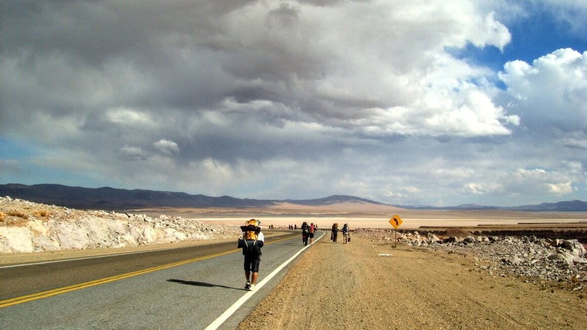 Backpackers hitchhiking on the road in atacama desert, Chile.