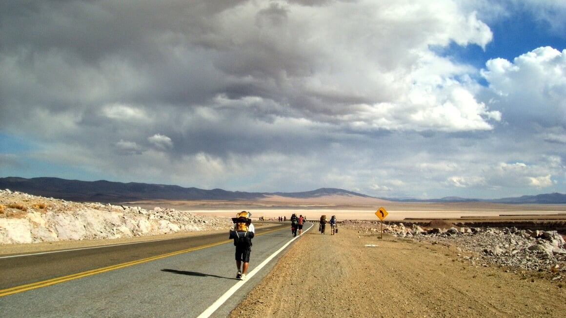 Backpackers hitchhiking on the road in atacama desert, Chile. 