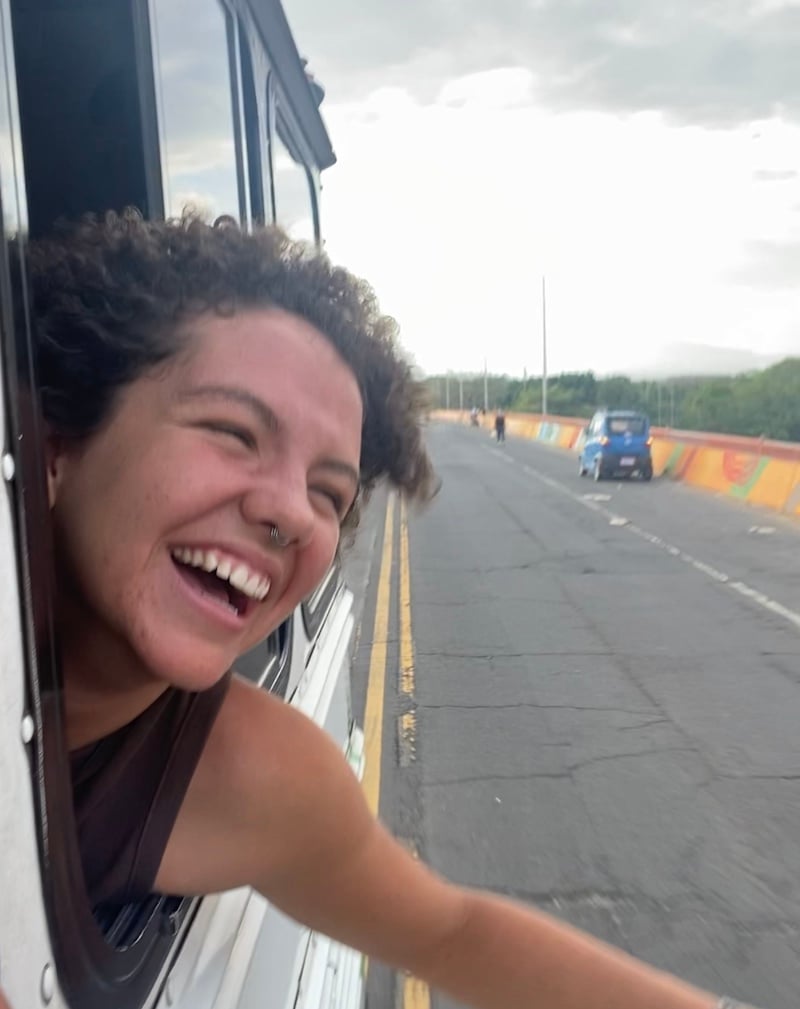 Girl smiles as she hangs out bus window in El Salvador.