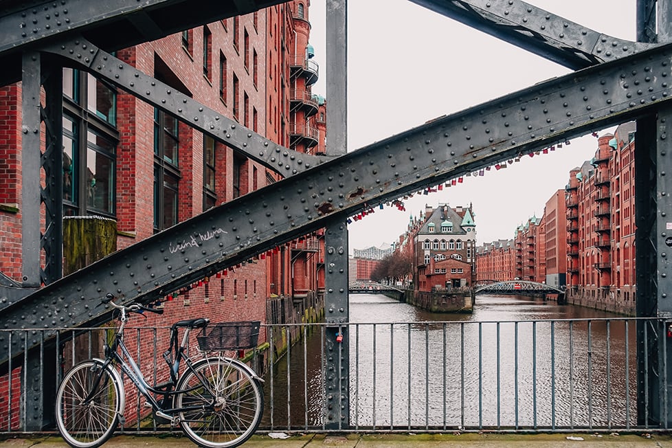 red brick warehouses on the canals of Hamburg taken from an iron bridge with a bike leaning against it.