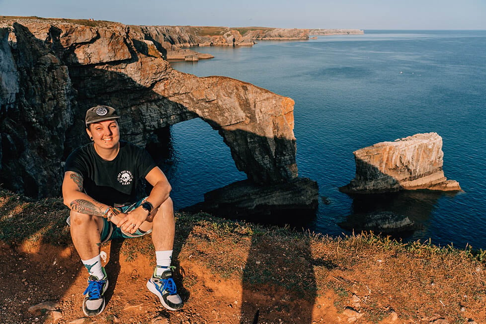 A person sat on a cliff in front of a sea stack on the Welsh course.