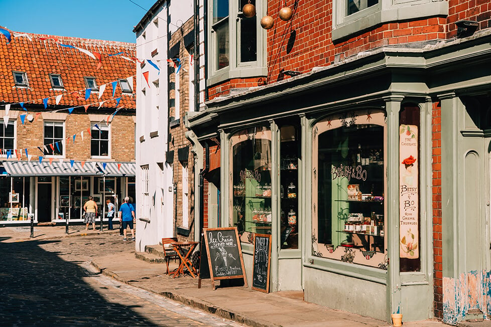 A typical English village bathed in sun with bunting hanging between the shops