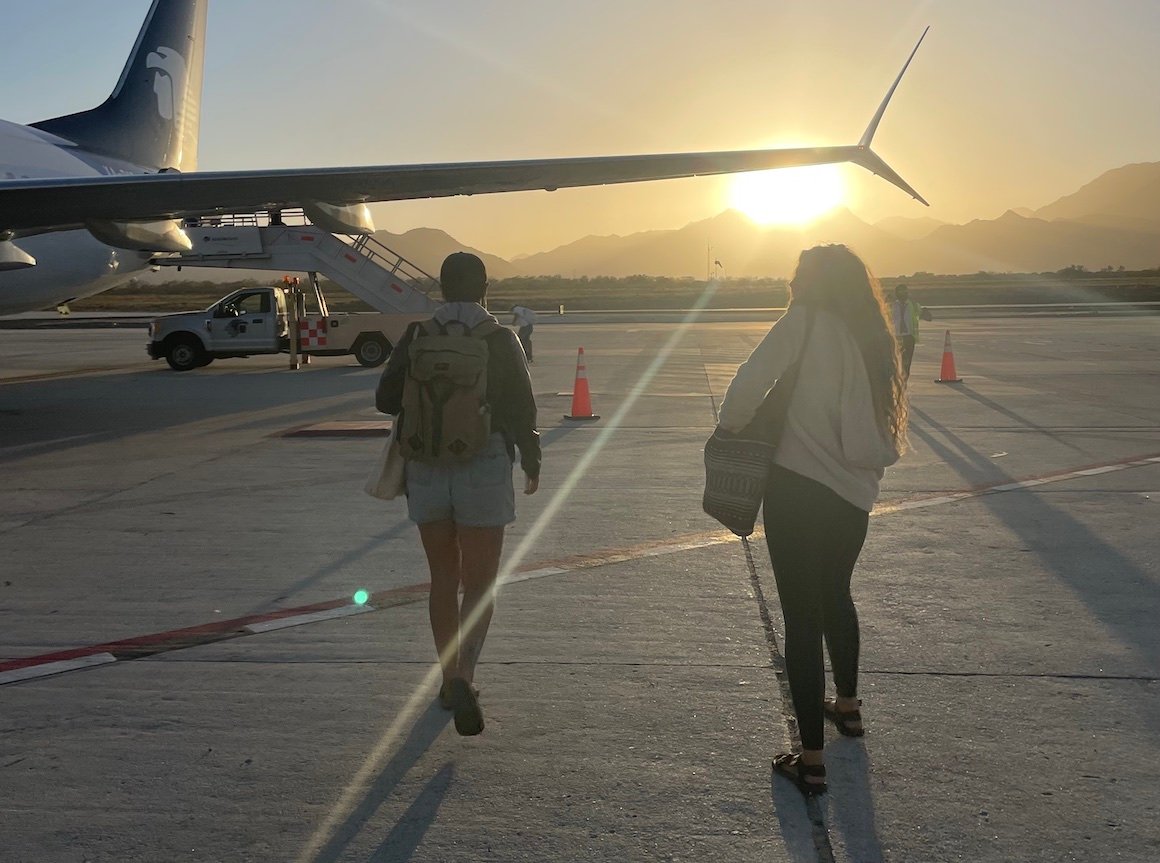 Two girls walking towards a plane at sunset in Mexico