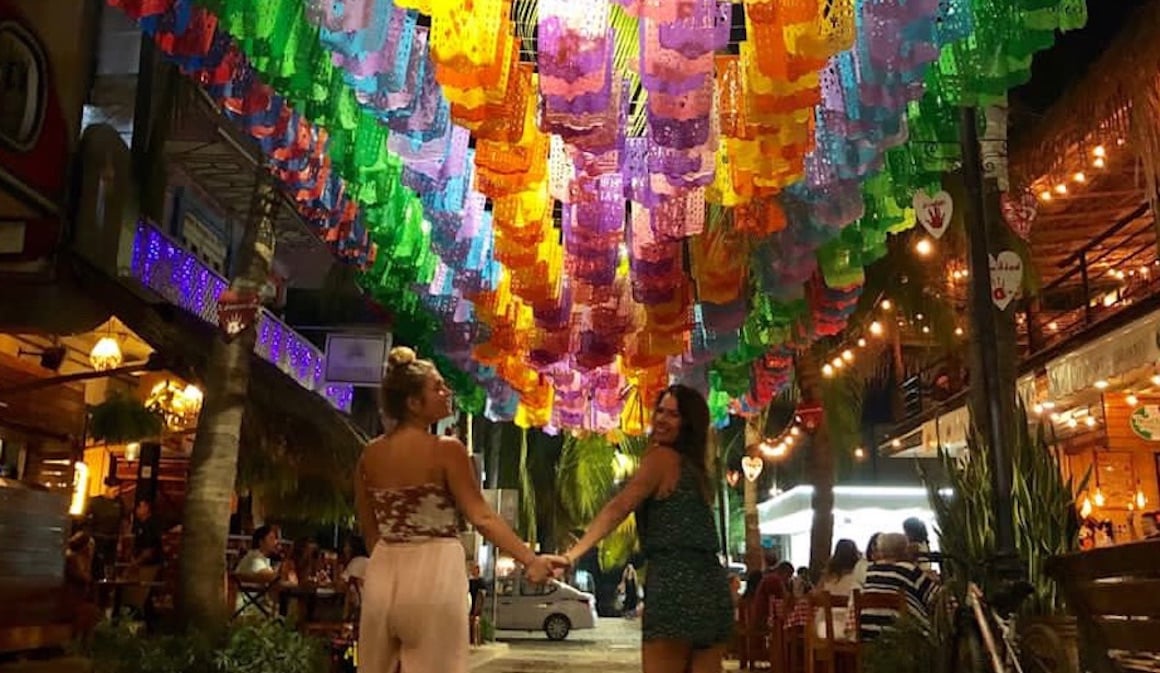 Two girls holding hands under the vibrant Mexican flags that line the streets of Sayulita.