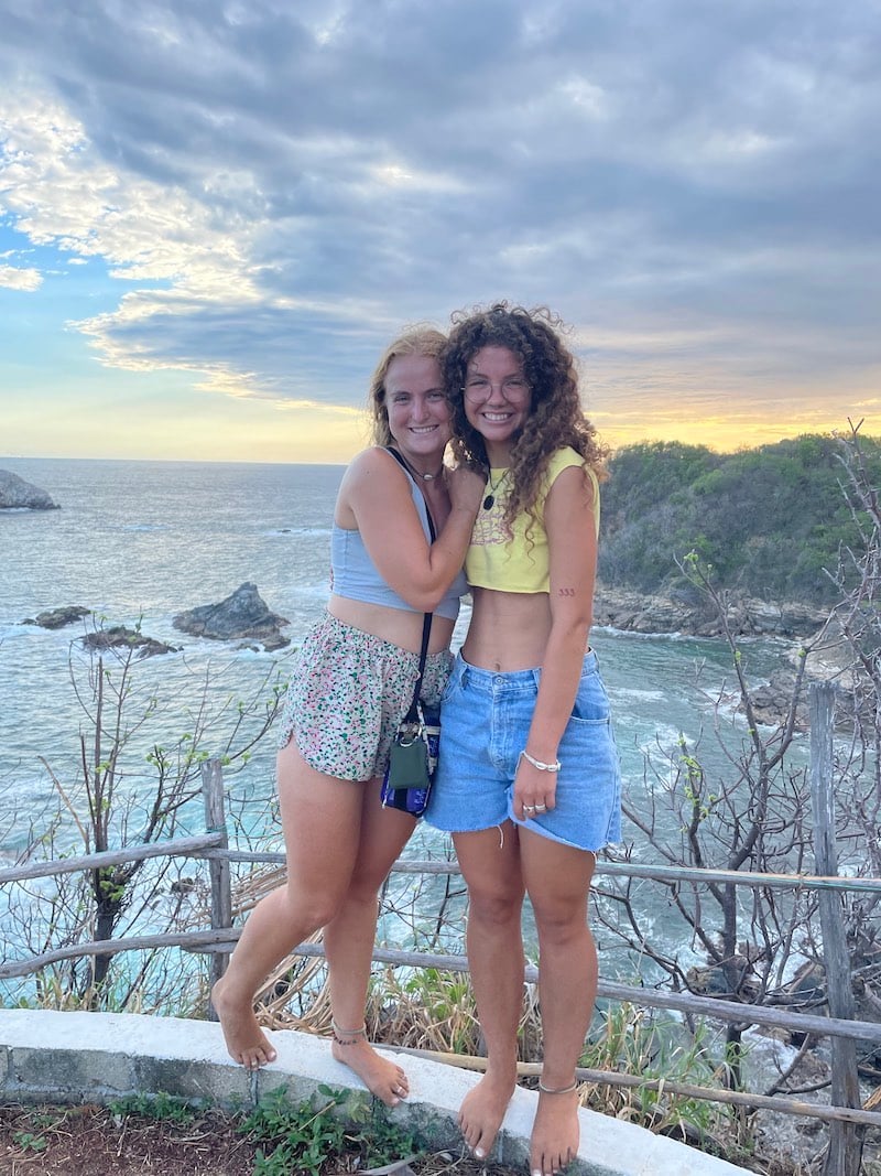 Two girls smiling next to a beautiful cliffside in Zipolite, Mexico.