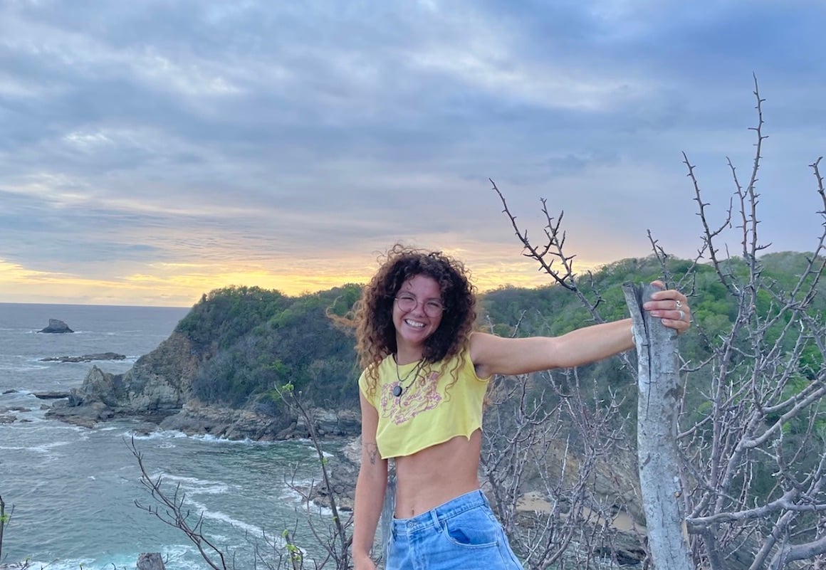 Girl smiles cheerfully as she stands on a cliff overlooking a beach in Zipolite Mexico.