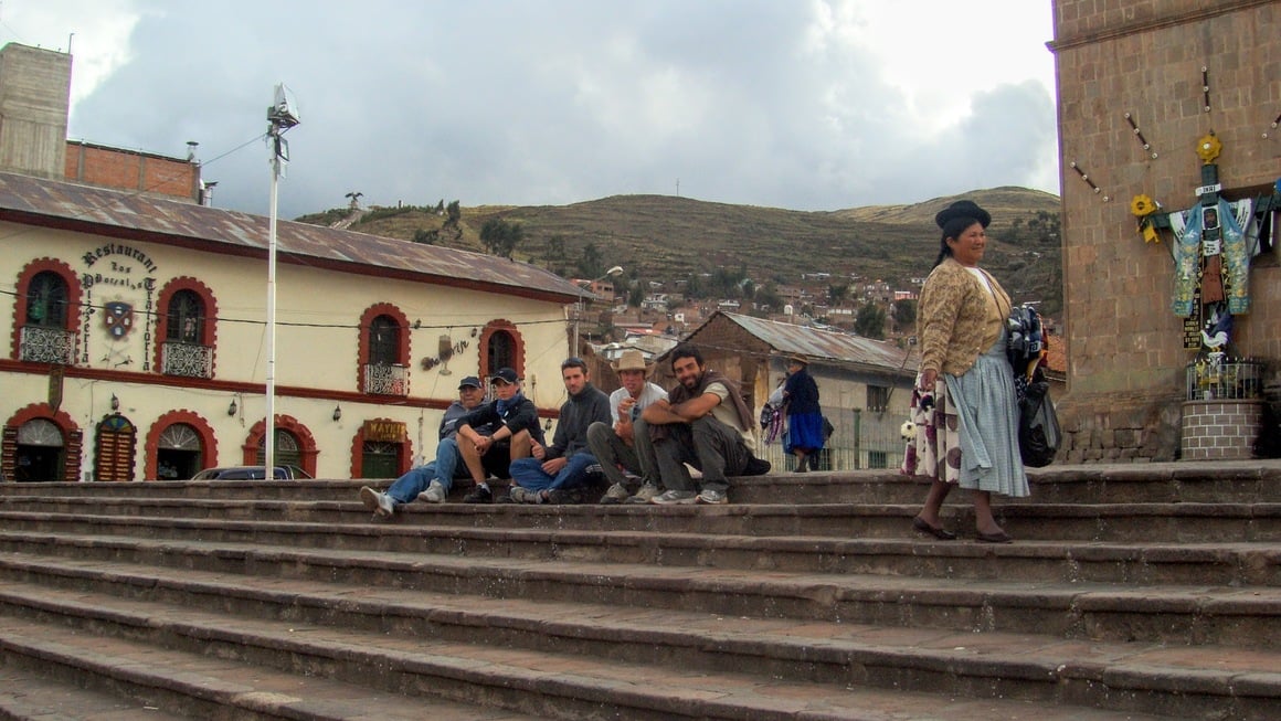 Backpackers relaxing on cuzco main square while local lady pass by.