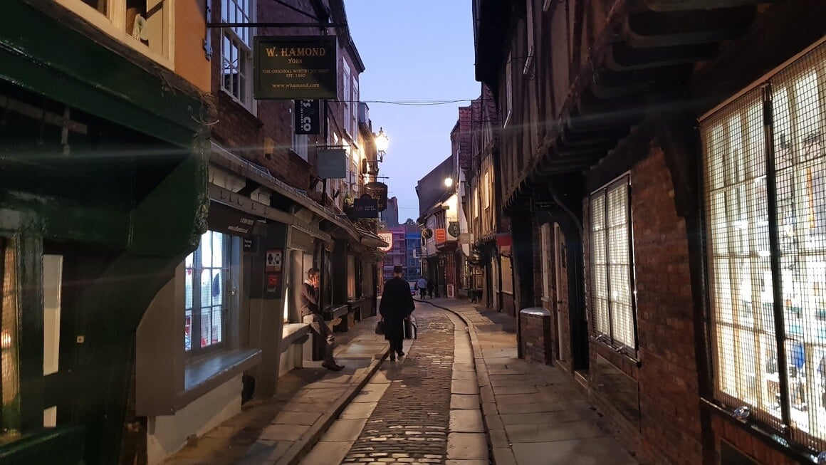 cloaked man walks down an old english cobbled street