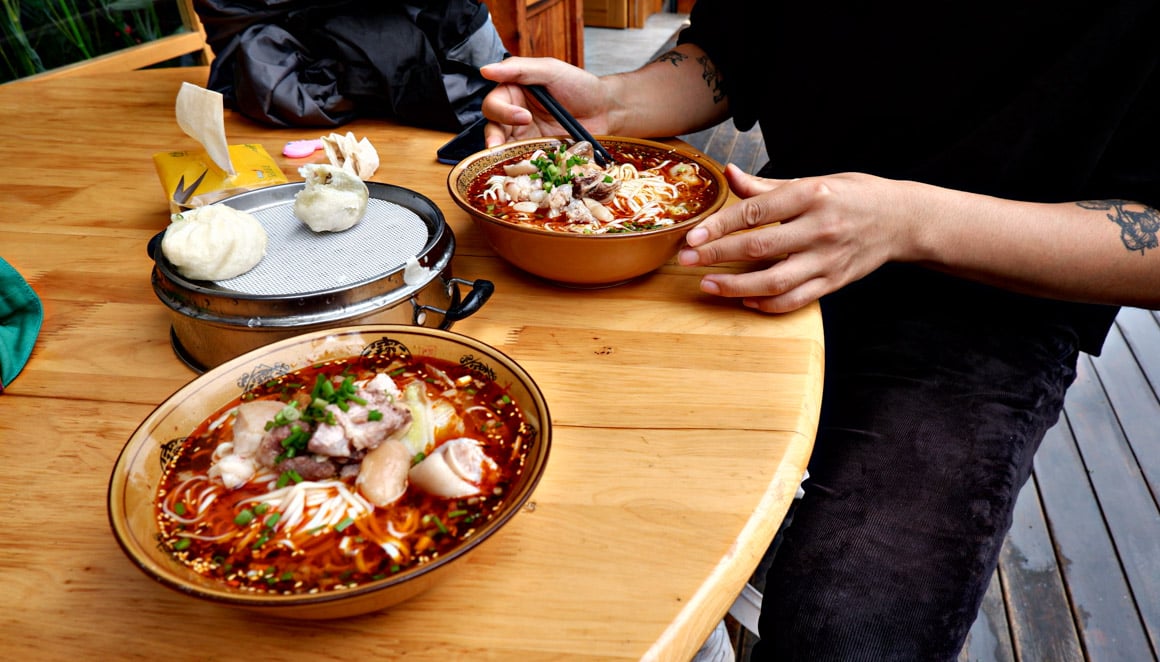 A bowl of spicy pork knuckle noodles and some steamed bao buns