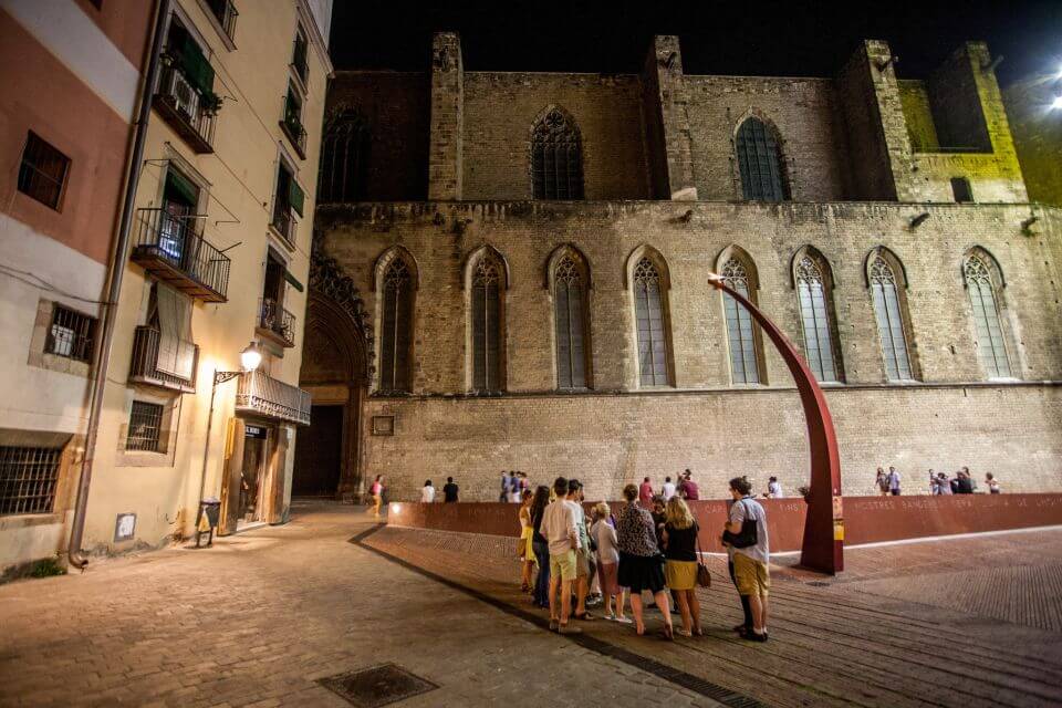 A group of tourists standing in front of the Fossar de les Moreres in Barcelona at night