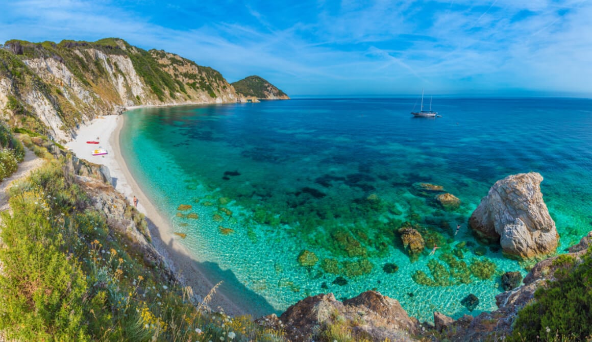 Beach in Elba, Italy surrounded by mountains with a boat floating in the water 