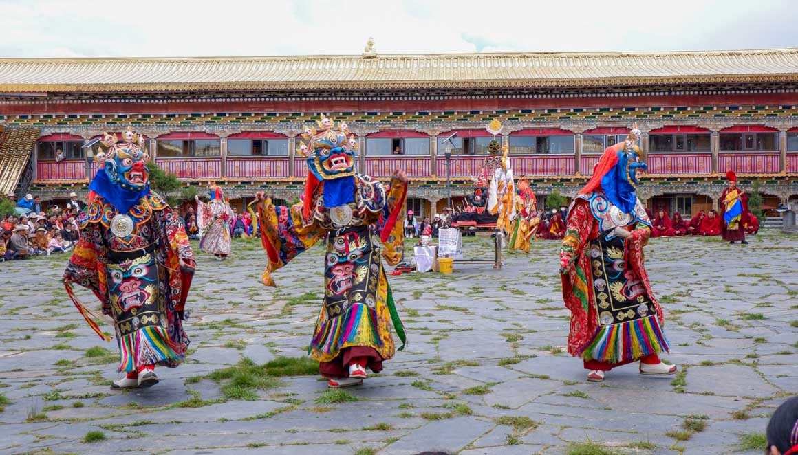 Three people wearing colourful Tibetan masks and doing a traditional dance