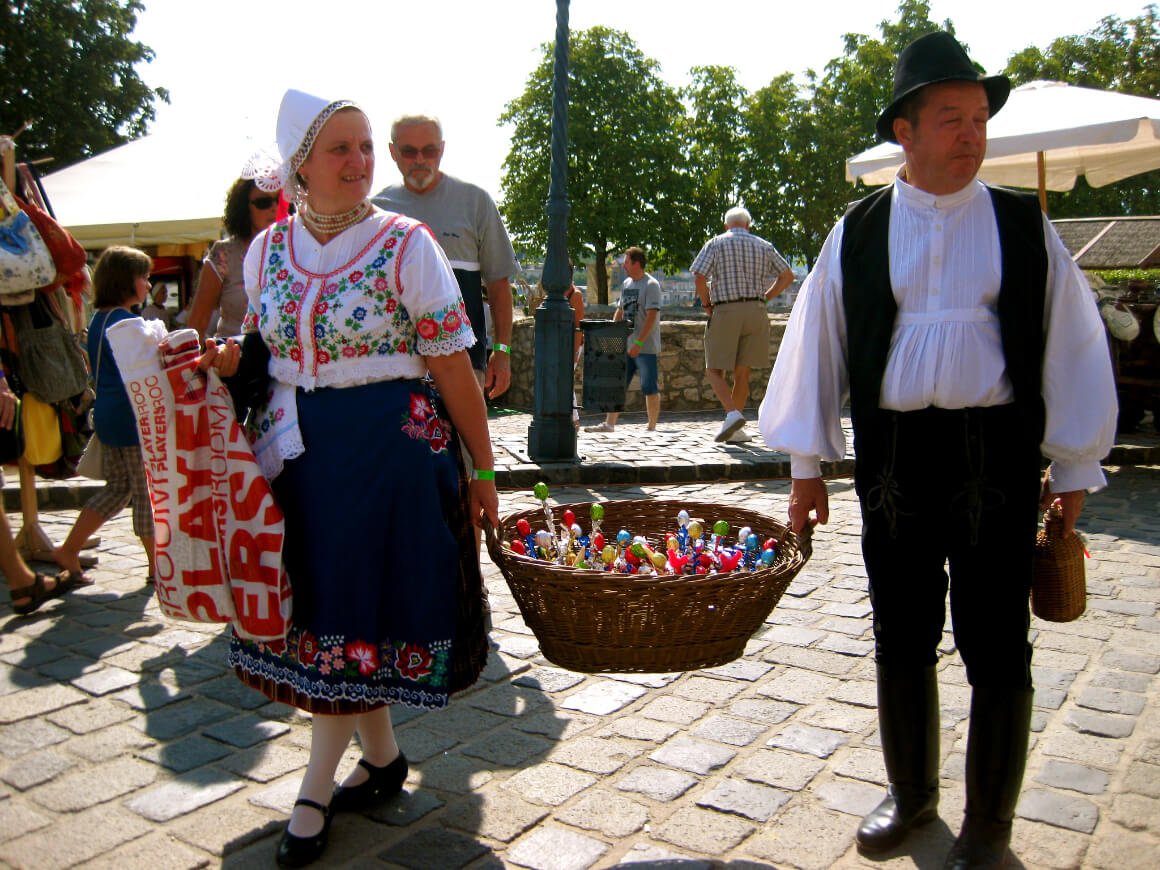 Two people carrying a basket wearing a traditional costume during the Festival of Folk Art