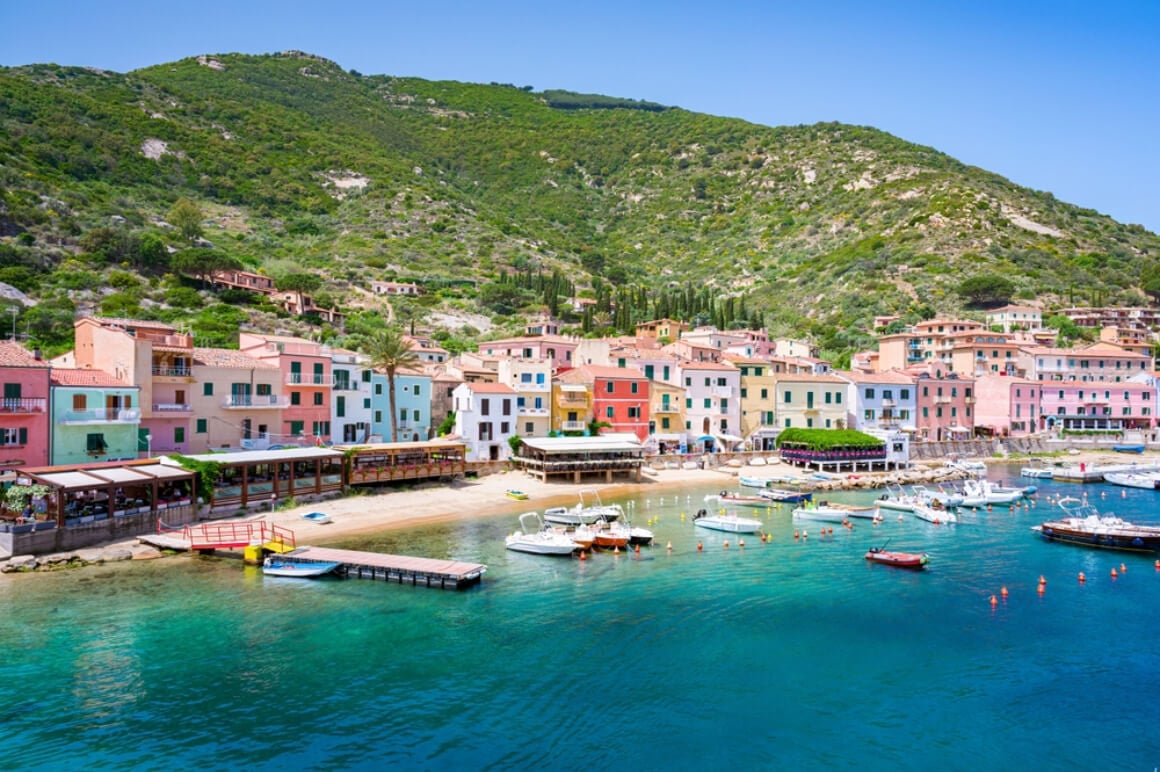 Colorful houses at the coastline of Giglio Island Italy with boats afloat and mountains in the background