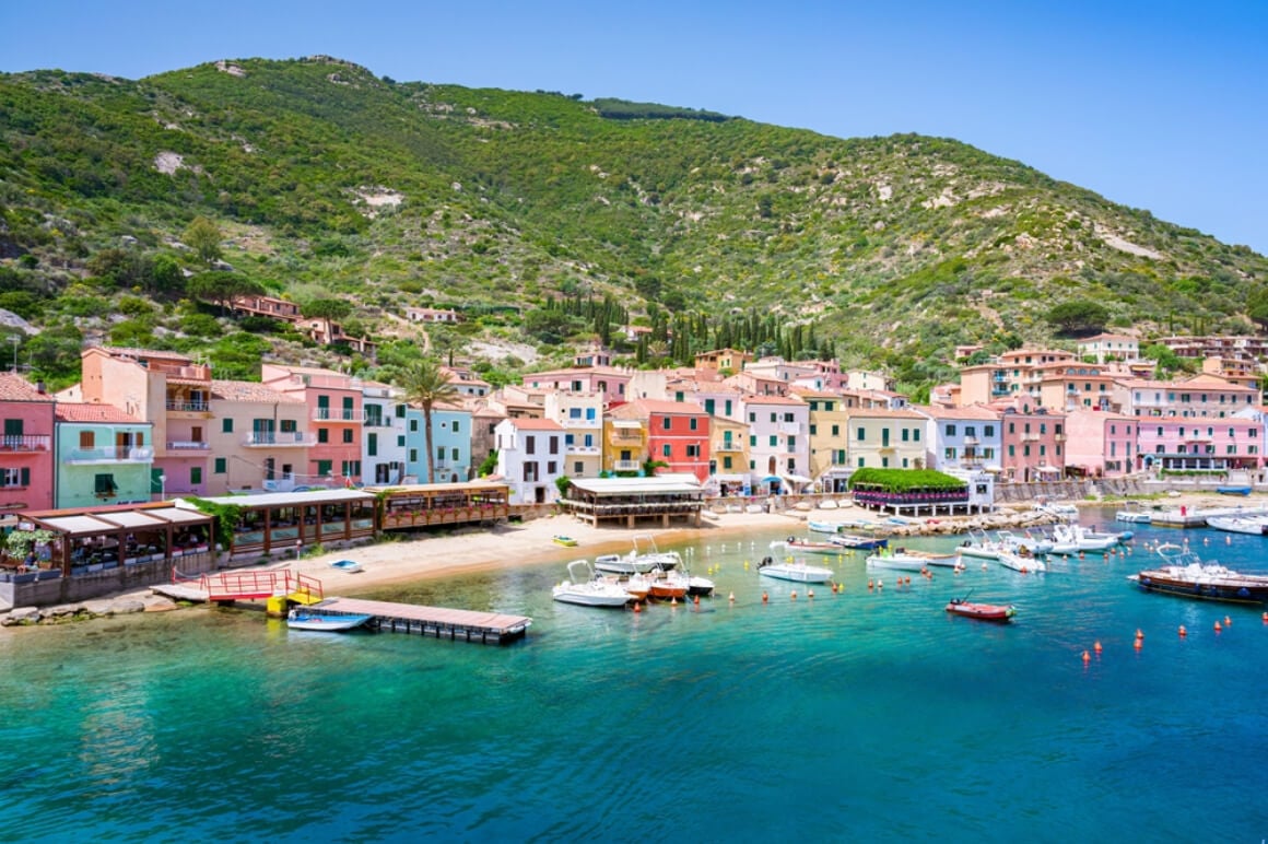 Colorful houses at the coastline of Giglio Island Italy with boats afloat and mountains in the background