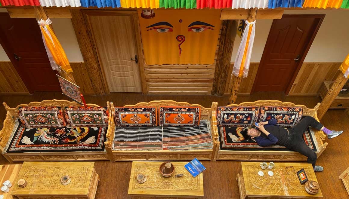 A man lies on a couch in a room decorated with wooden Tibetan furniture