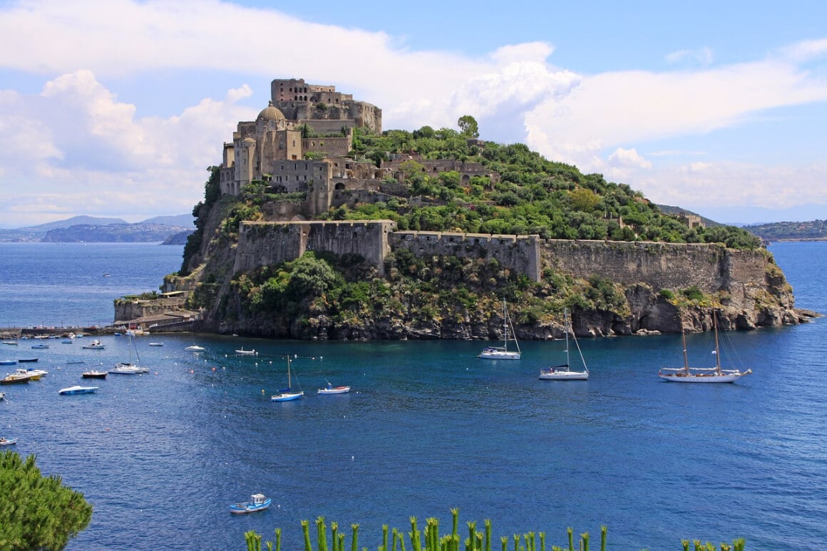 small island in the middle of the sea with a castle on top and surrounded by boats in Italy