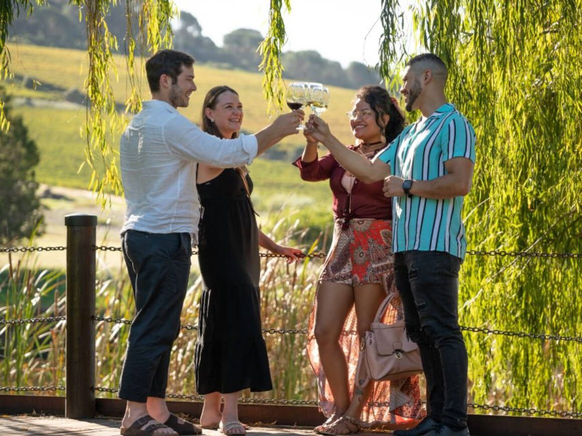 four people cheersing glasses of wine in a green vineyard