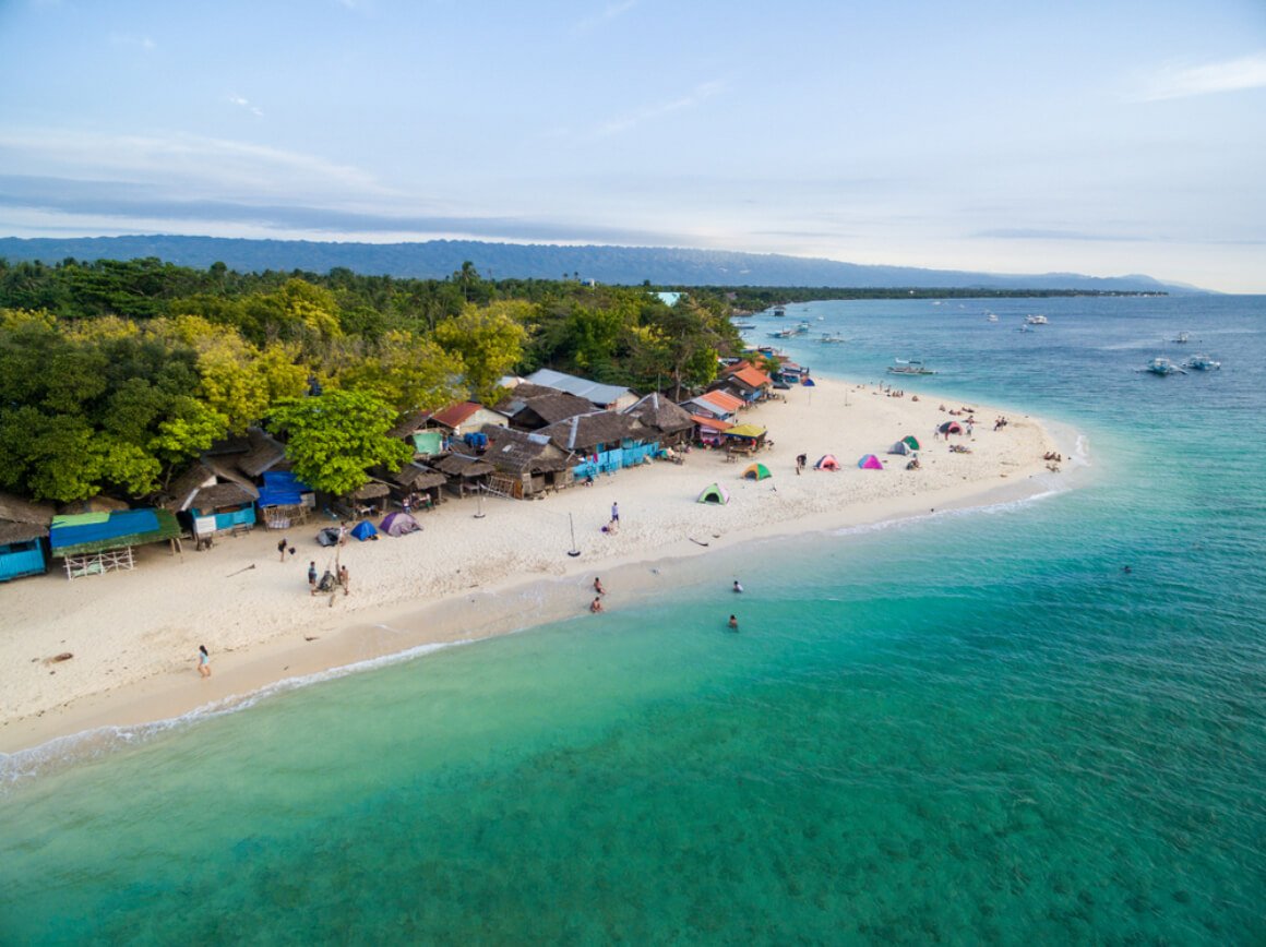 People swimming and cottages nestled along the coastline at the White Beach, Moalboal 