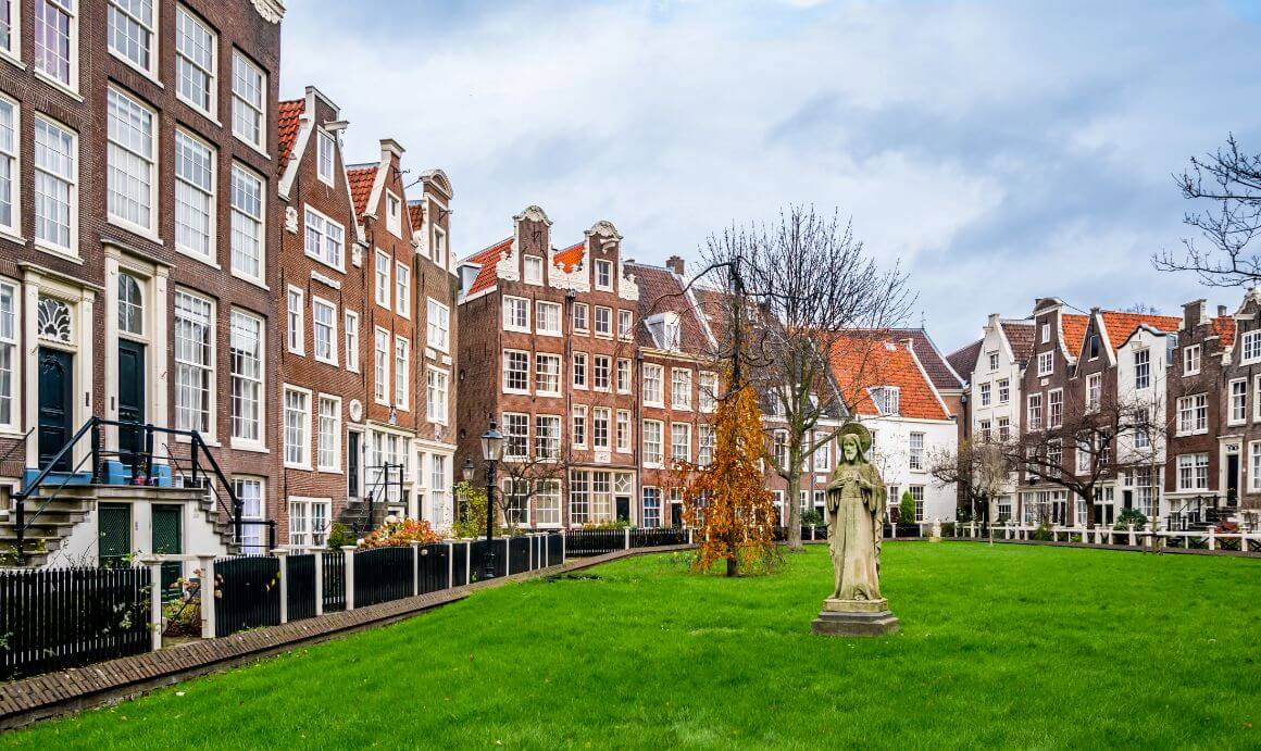 Begijnhof's garden surrounded by buildings with many windows and red roofs with a statue in the middle.