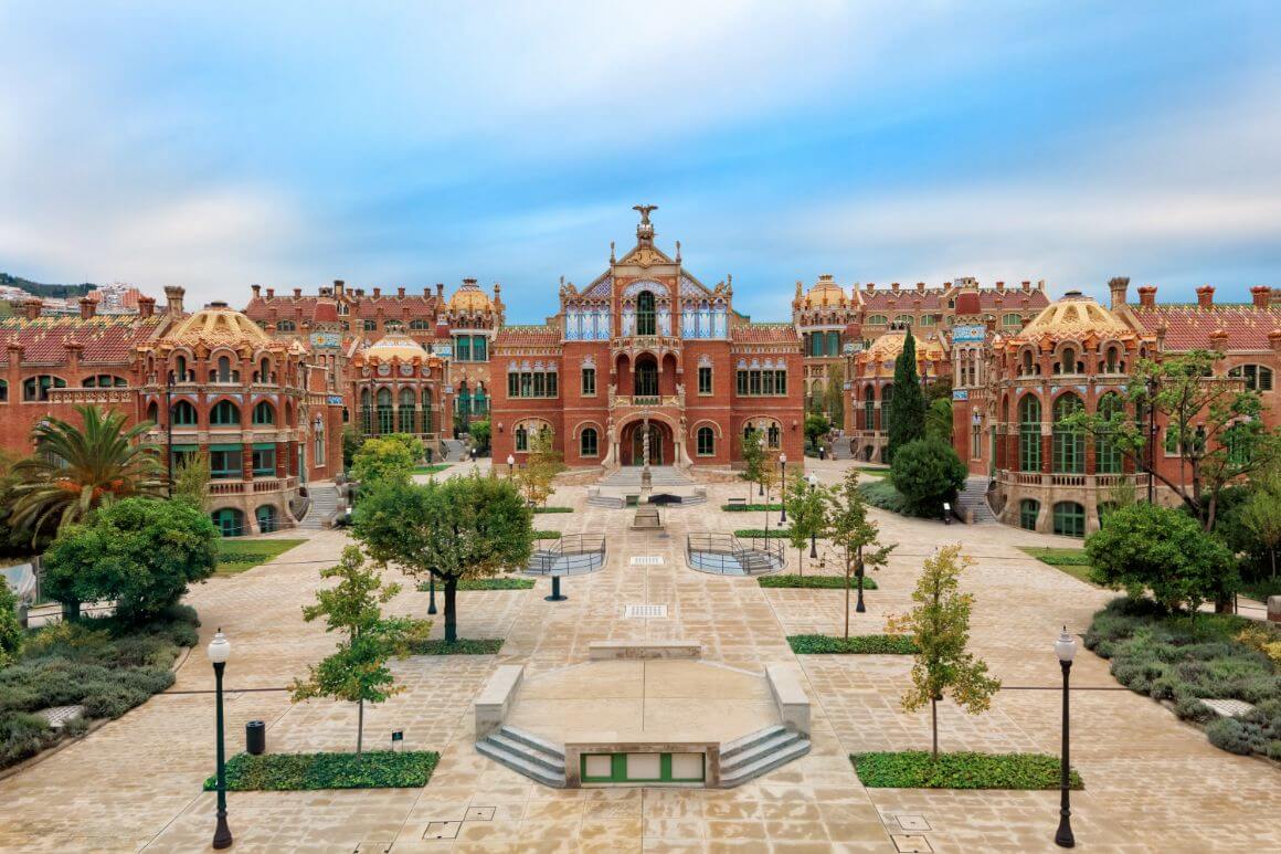 Brick and stone buildings and large courtyard adorned with trees and a fountain in Hospital de Santa Creu i Sant Pau, Barcelona