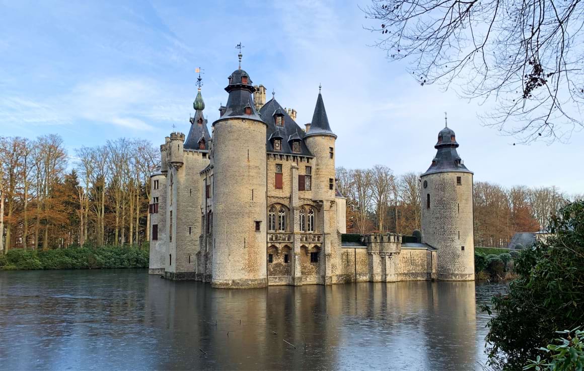 A medieval stone castle with towers stands on a small island in the middle of a large lake with trees in the background.