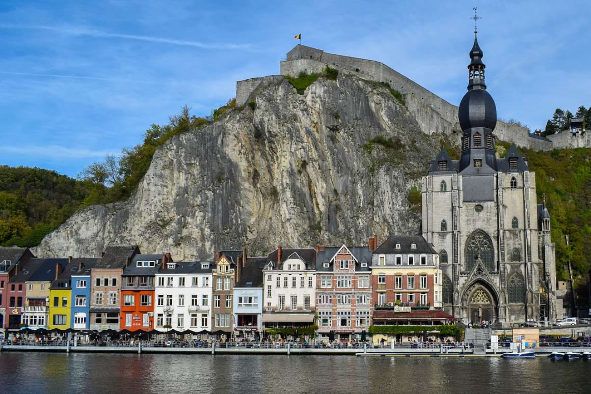 Buildings and a chirch aligned on the coastline of Dinant with a mountain in the backdrop