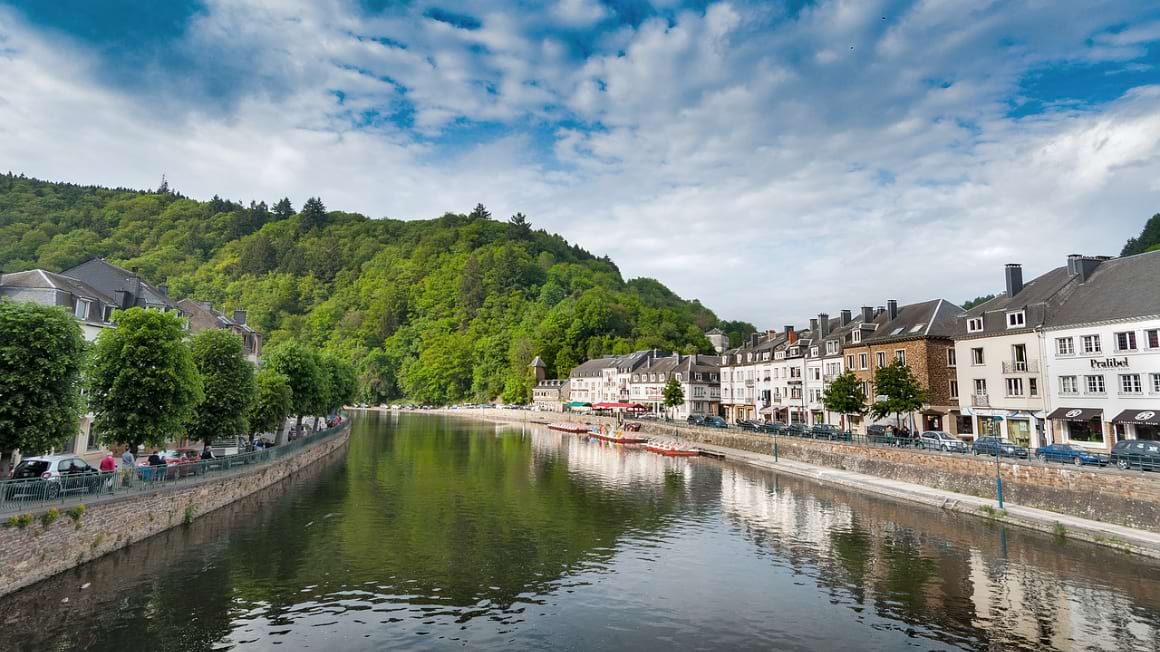 A lake nestled among buildings with a lush forest in the backdrop in Wallonia, Belgium