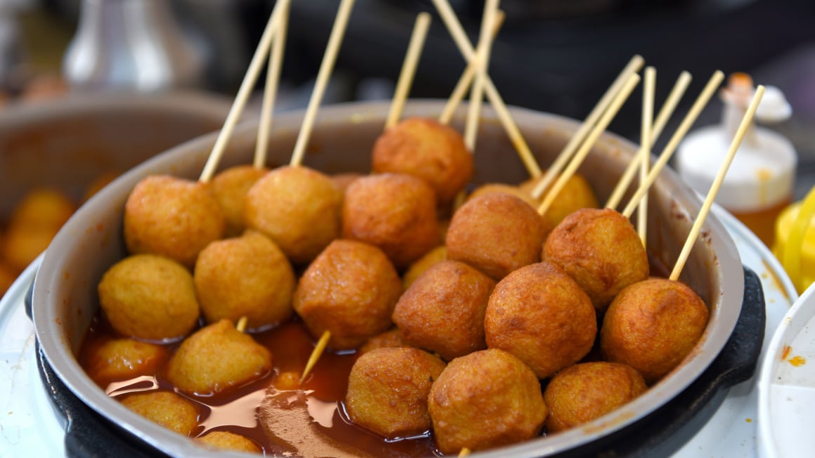 fried circular fihs balls on wooden sticks in a bowl