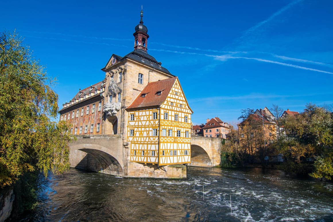 A building on top of a river surrounded by lush trees in Bamberg, Germany